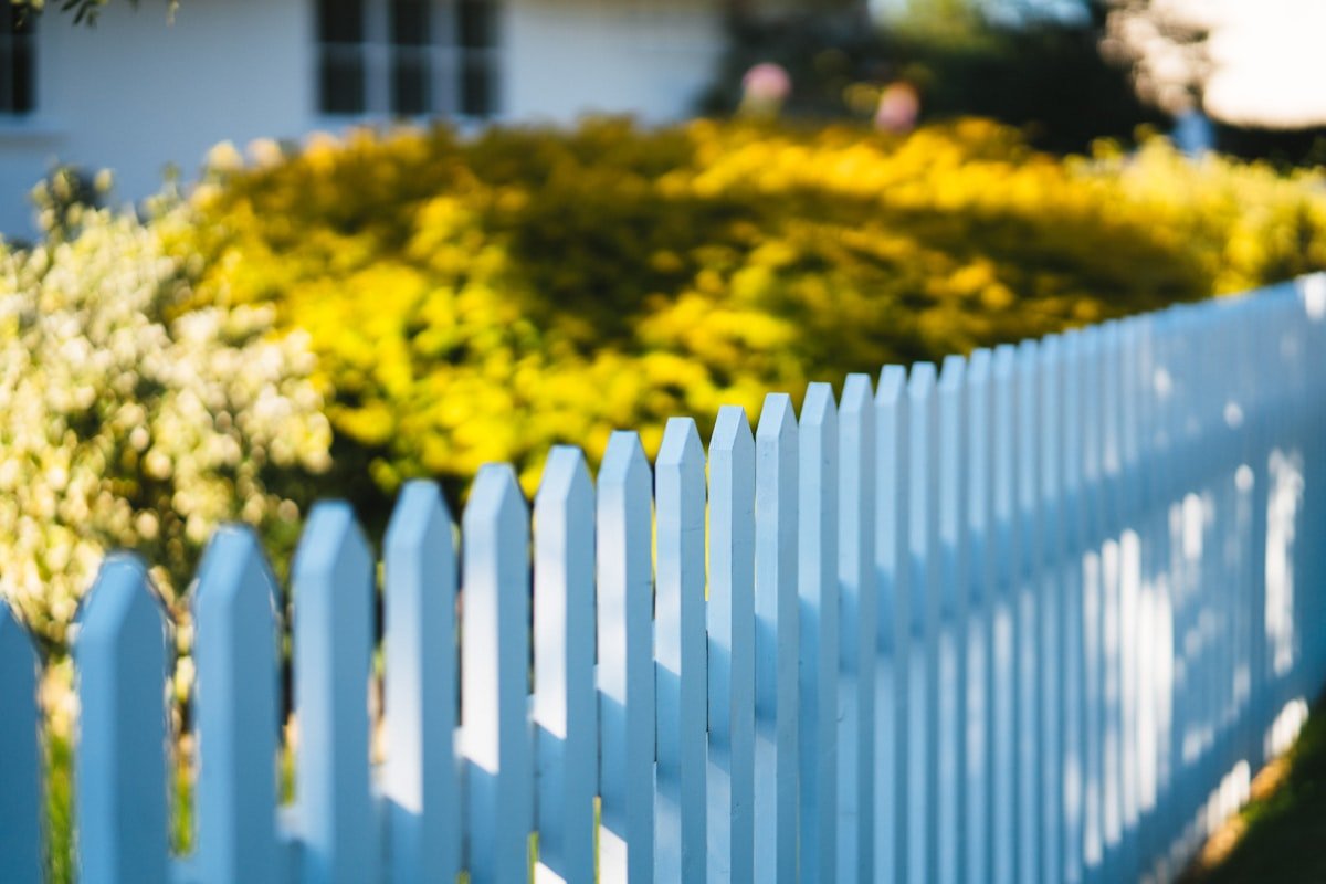 White picket fence in front of a house with a green lawn